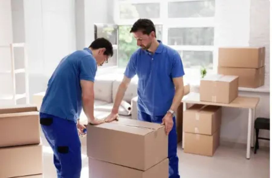 Two men in blue uniforms carefully packing and handling boxes in a well-lit room, preparing for a move.