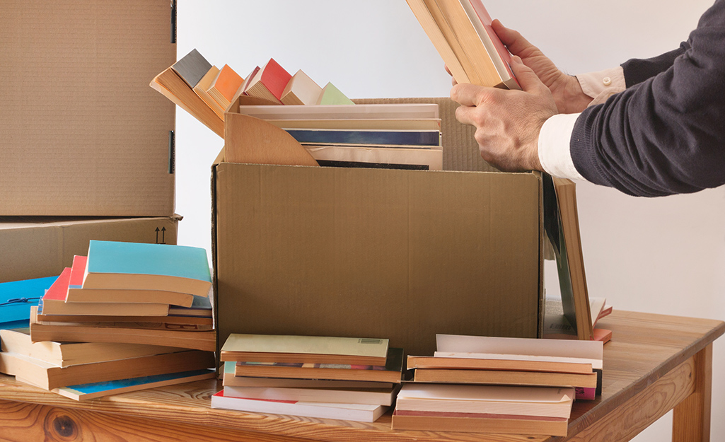 Someone packing books into a cardboard box, with more books stacked nearby, demonstrating how to organize and pack books for a move.
