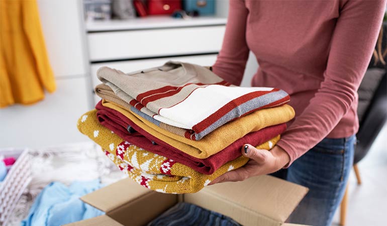 A person holding a stack of neatly folded clothes, preparing to pack them into a box for a move.