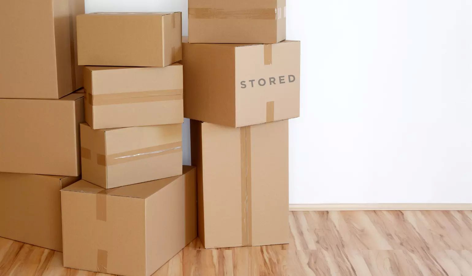 Stacked cardboard boxes labeled 'STORED' against a white wall, suggesting a moving or storage process.