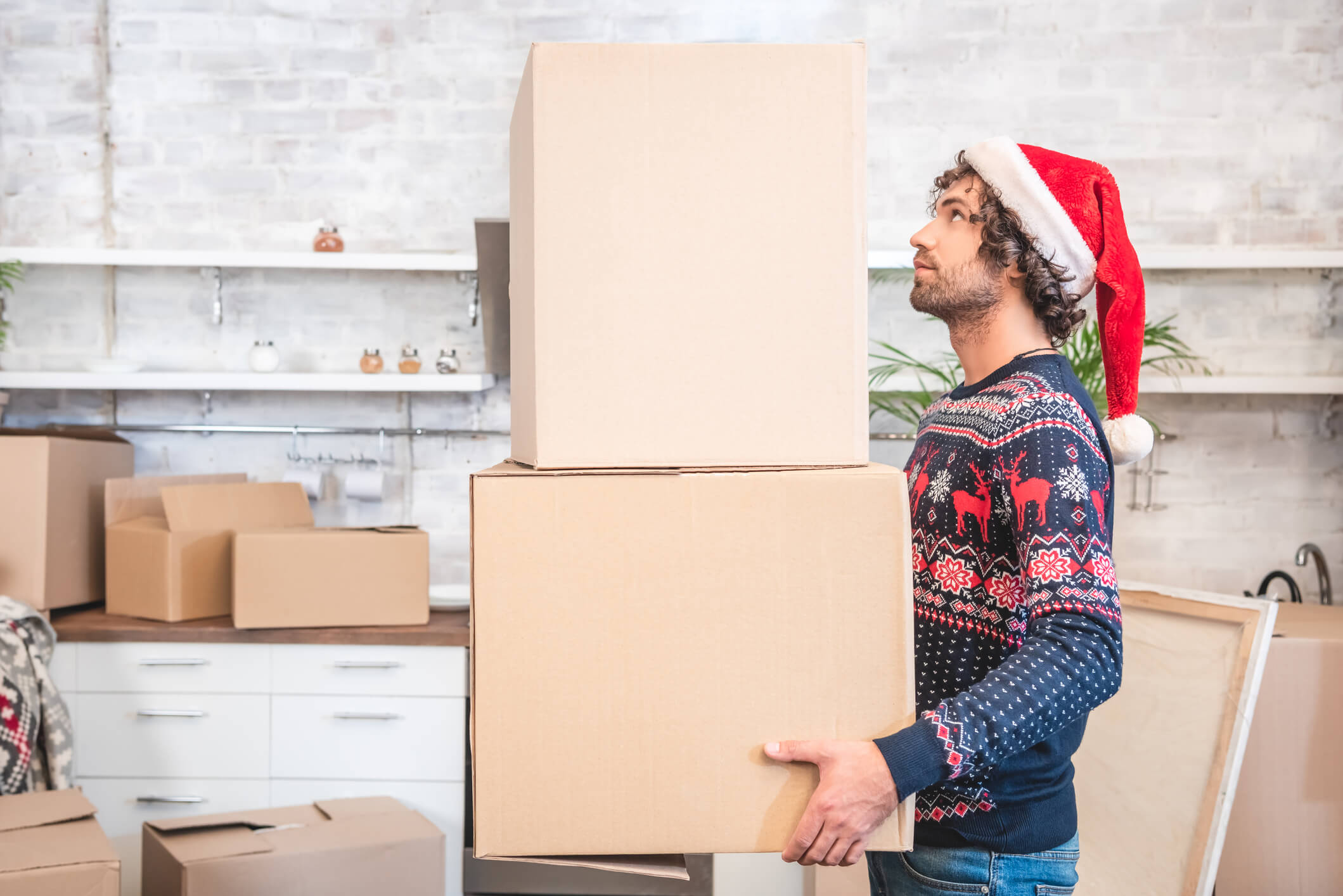 A person holding two moving boxes while wearing a Santa hat